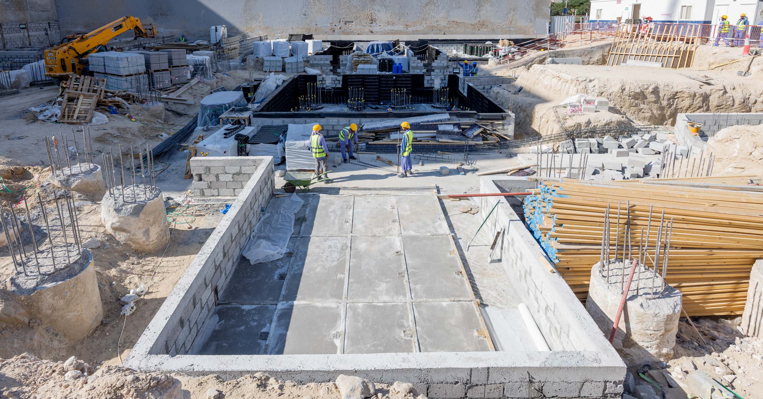 Pearl House By Imtiaz Construction site with workers in helmets, machinery, concrete structures, and building materials visible.